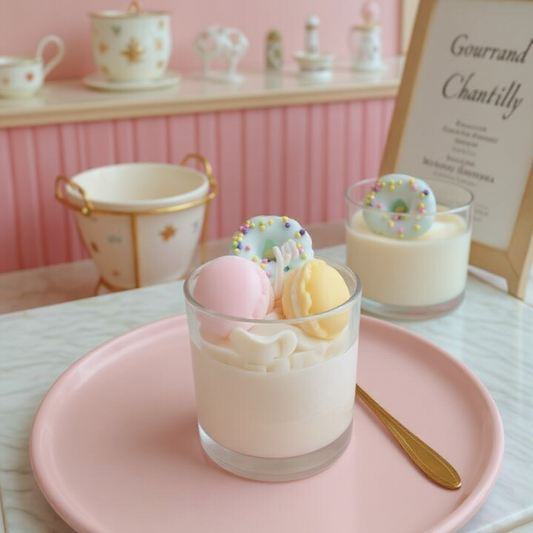 Bougie effet chantilly réaliste en cire, ornée de macarons roses et jaunes et d’un donut bleu pastel.