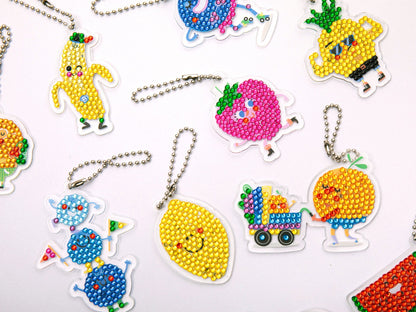 Détail des strass colorés en cours de pose sur un porte-clés fruit.